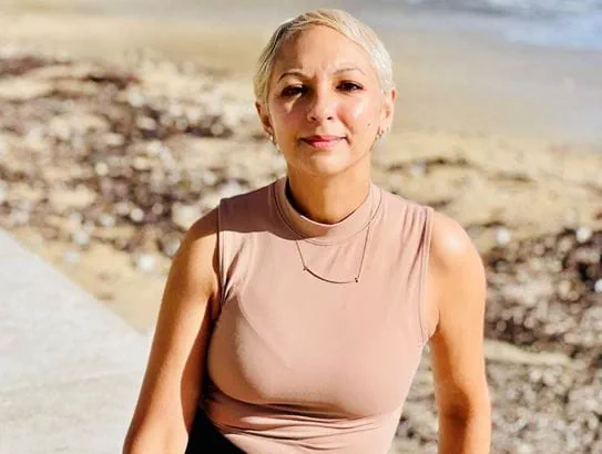 Nalini Sharma sitting on a beach shore.