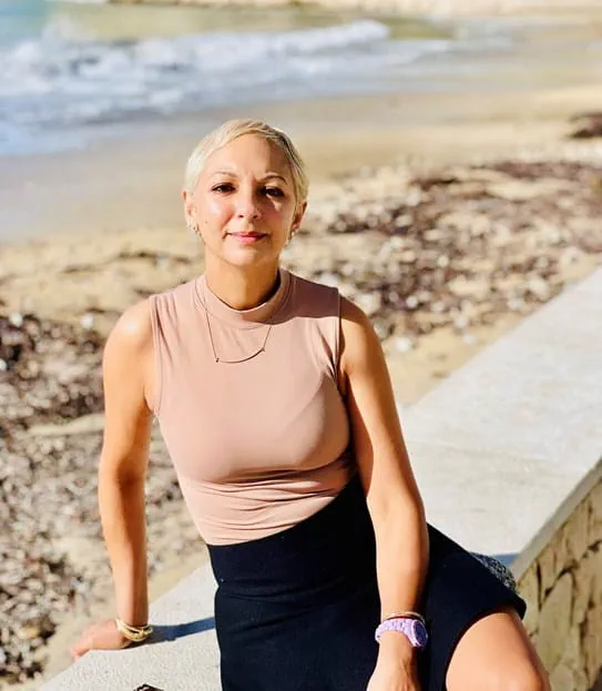 Nalini Sharma sitting on a beach shore.