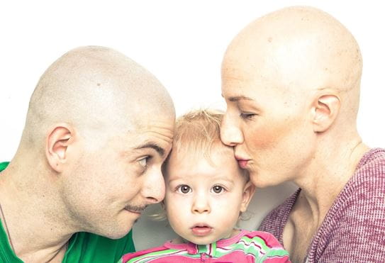 Corinne with her husband with a shaved head and kissing her son in the middle.