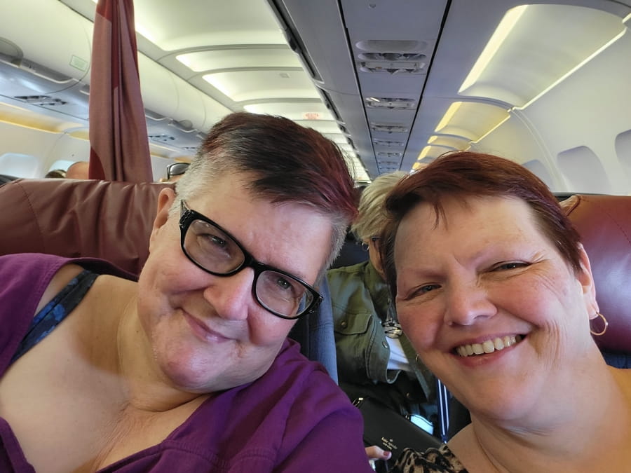 Paula and Sandra sitting on a plane and smiling at the camera.