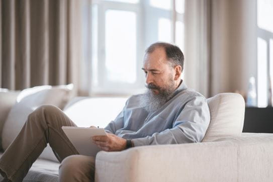 A man sitting on a couch and writing in on a pad of paper.