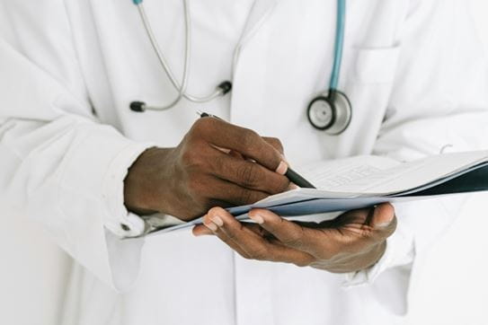 A doctor wearing a stethoscope and lab coat, writing in a chart.