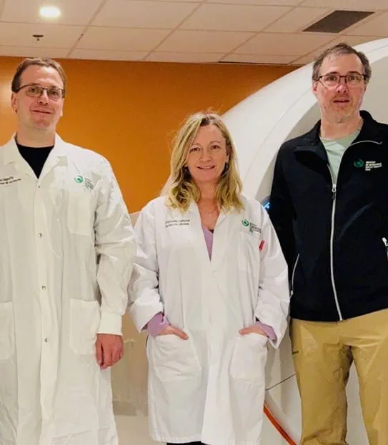 Dr Eric Turcotte and his team stand in front of a scan machine.