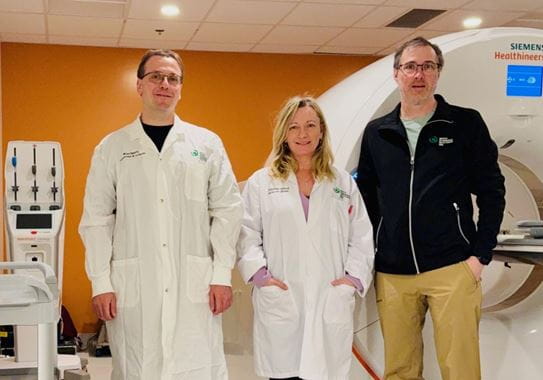 Dr Eric Turcotte and his team stand in front of a scan machine.