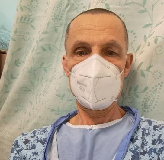 Ron wearing a face mask and a hospital in front of a curtain.