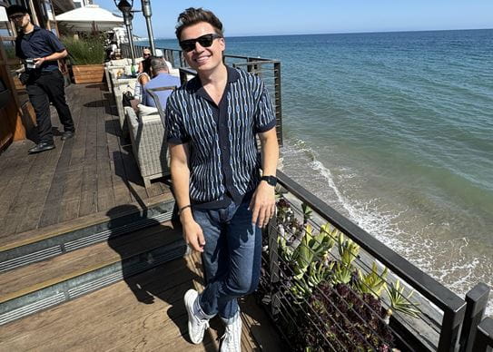 Shawn Hook wearing sunglasses and smiling while standing next to a body of water.