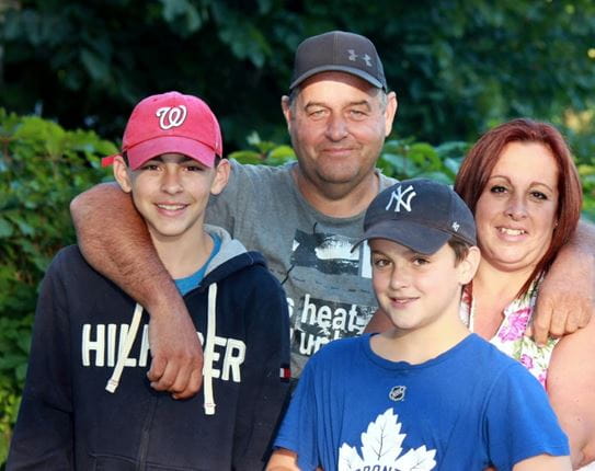 Annie Lemieux sourit et pose devant des arbres avec son conjoint et ses deux fils.