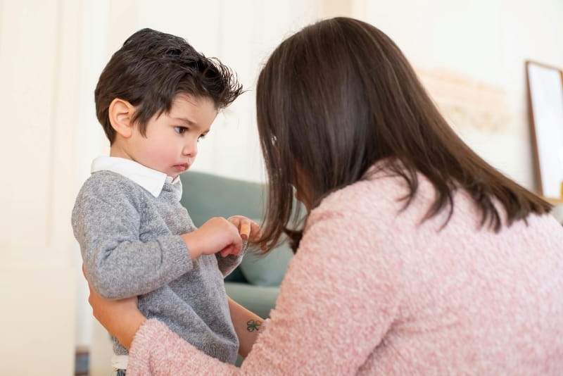 A woman sitting in front of a toddler and holding him by the waist.