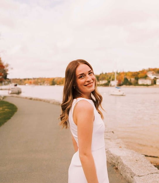 Ruby, souriant en se retournant pour faire face à l’appareil photo, sur une voie piétonne au bord d’un lac.