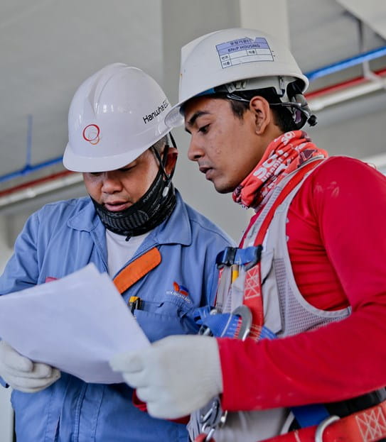 Two people wearing hard hats and reading a piece of paper.