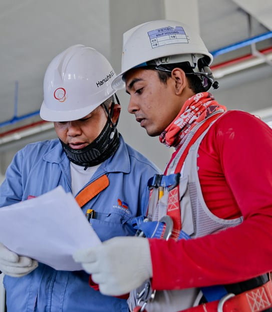 Two people wearing hard hats and reading a piece of paper.