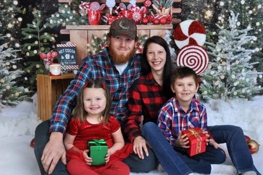 Kayla Ouellette, her children and partner, Cyle smiling and sitting in front of a holiday display.