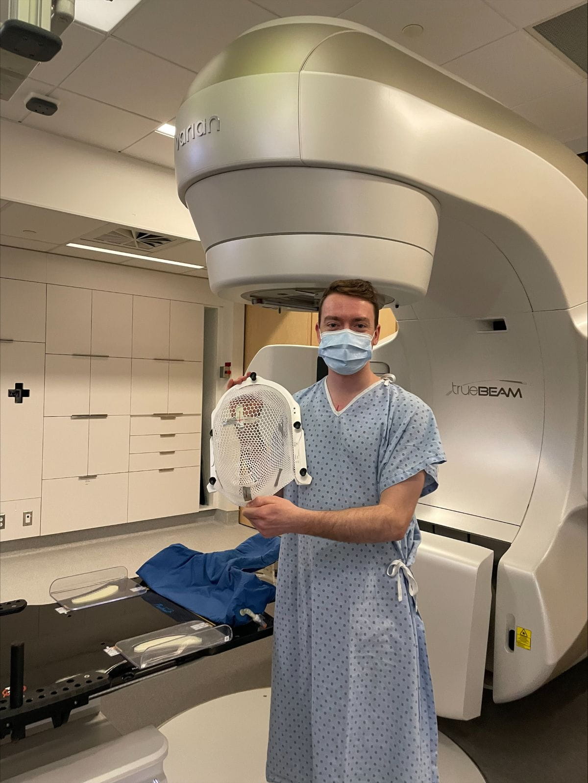 Anthony Vallée in a hospital gown standing next to a medical machine. 