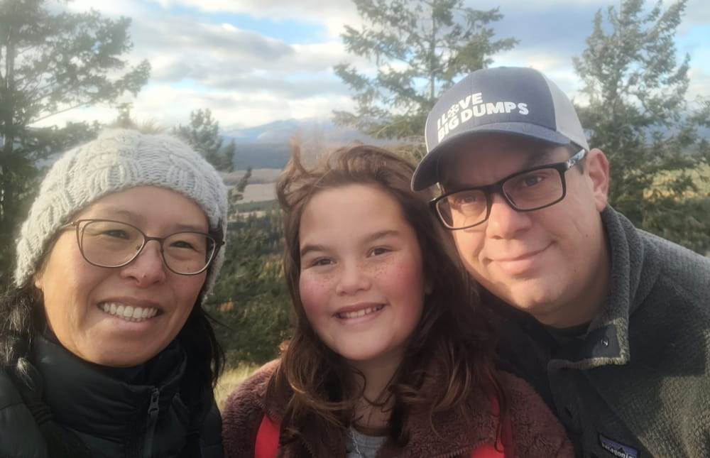 Rita, her daughter and husband smiling with trees in the background.