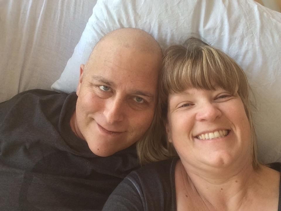 Chantal Tardif and her husband lying in bed, smiling at the camera.