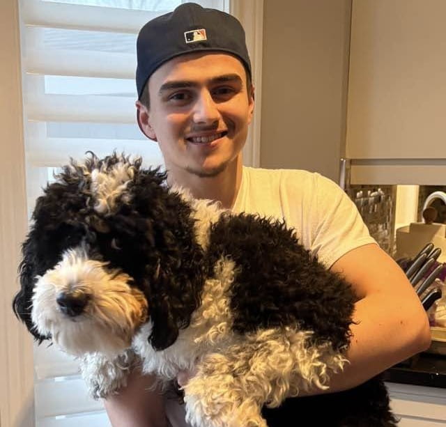An adult Aidan smiling and holding a dog.
