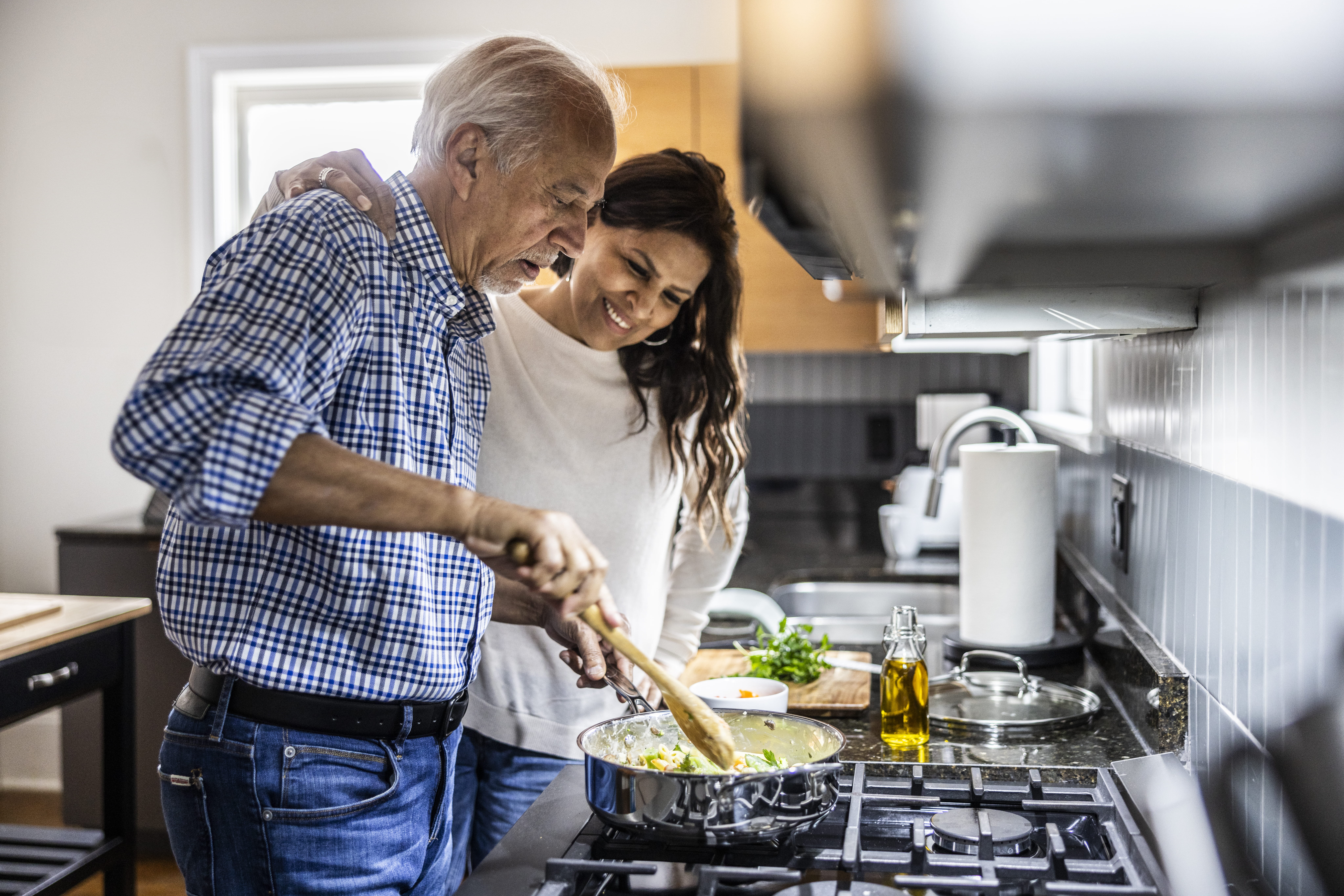 Two people cooking together stirring a pot on the stove.