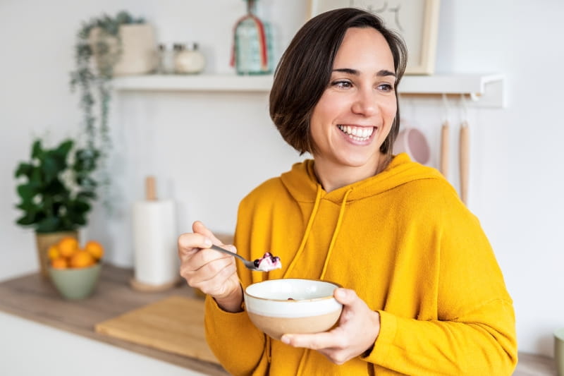 A person smiling and using a spoon to eat from a bowl.
