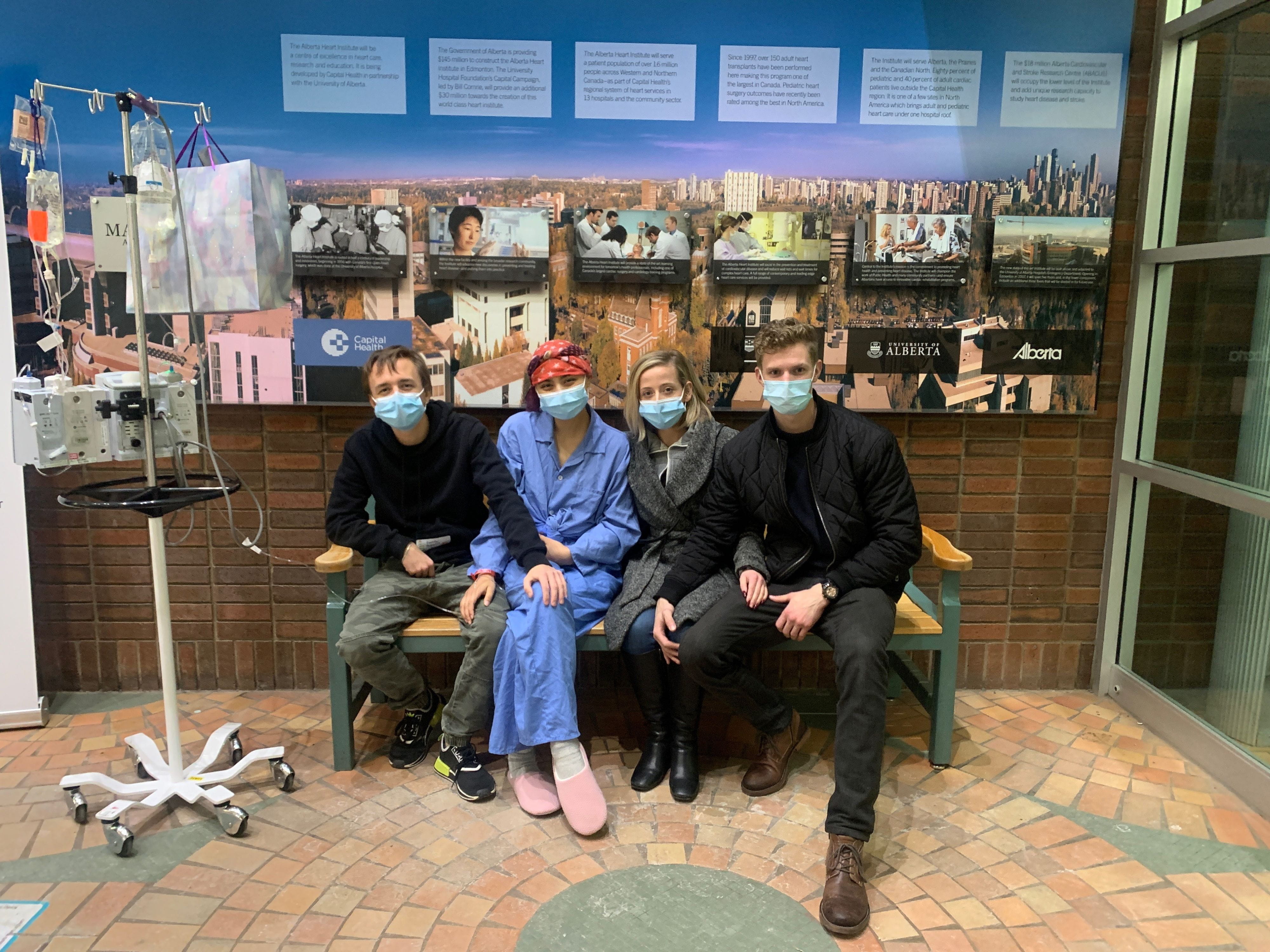 Caitlin est assise sur un banc à l’hôpital avec trois amis. Tous portent un masque et Caitlin est branchée à une perfusion intraveineuse.