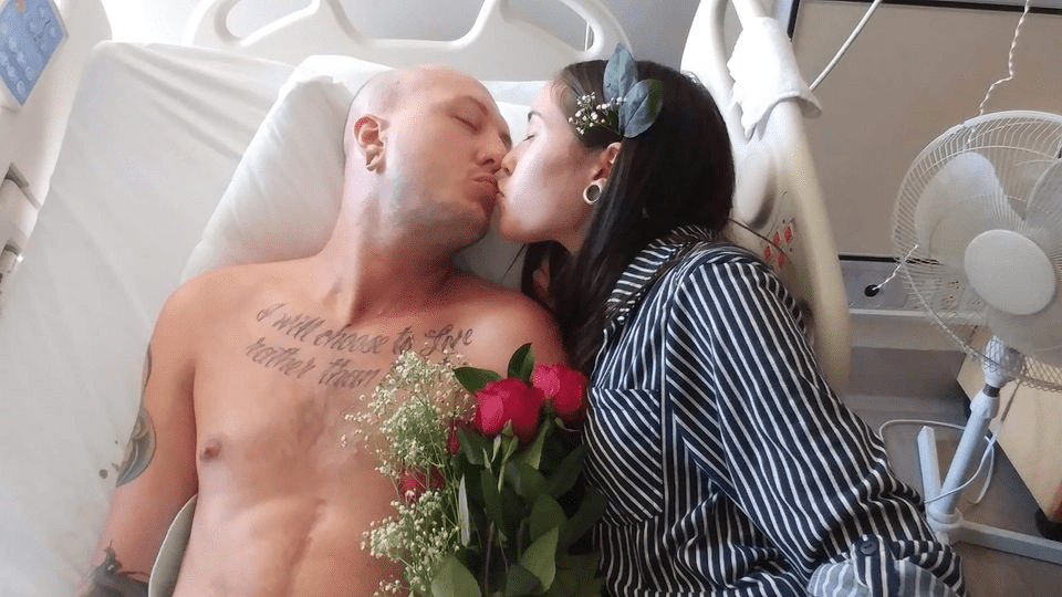 Nick and his wife kiss in a hospital bed after getting married.