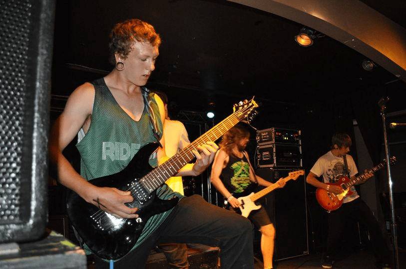 Nick plays the guitar on stage with his band.