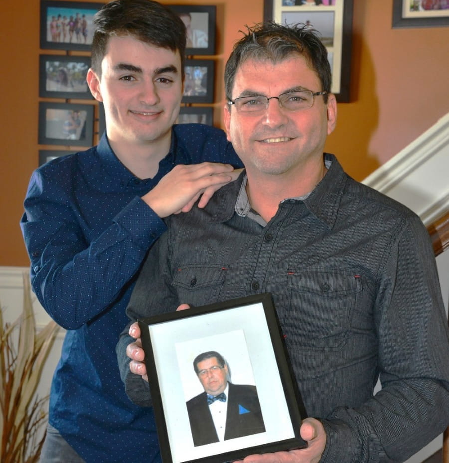 Denis and his son smiling while Denis holds a framed photo of his father.
