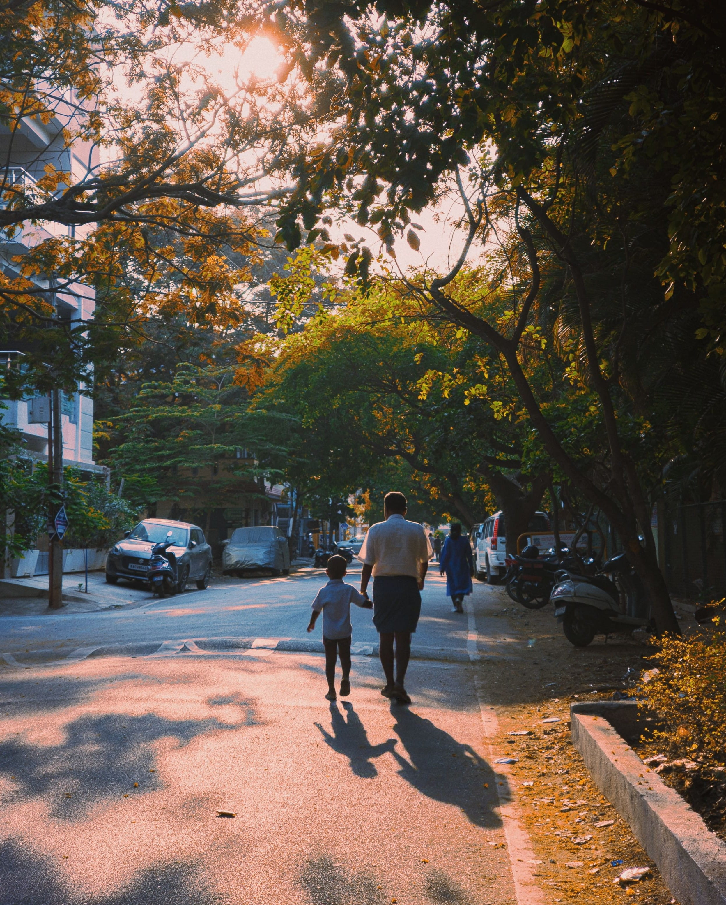 A father and a son holding hands while walking down a street.
