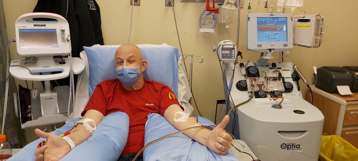 Terry lies in a hospital bed connected to different machines. He is showing 2 thumbs up. 