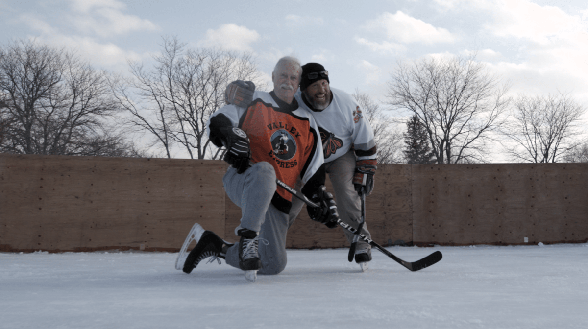 Stuart kneels on the ice while playing ice hockey with his son. 
