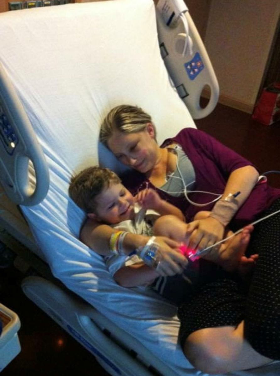 Catherine lies in a hospital bed cuddling with her son. 