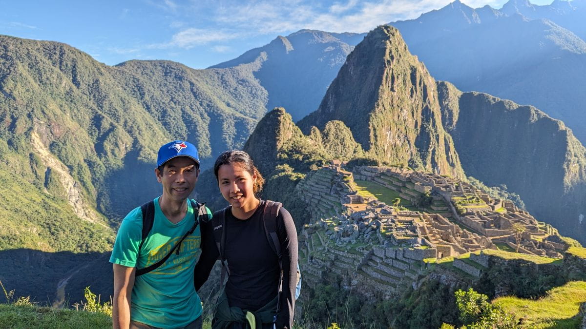 Winhan and his daughter smile in front of Machu Picchu. The sun is shining and there are mountains in the distance.