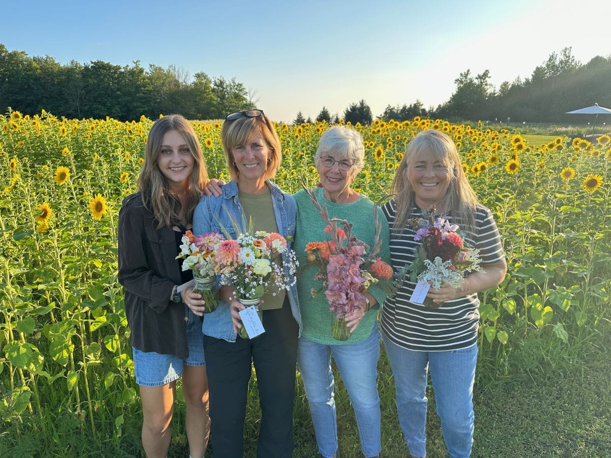Bonnie (troisième à partir de la gauche) se tient debout dans un champ de tournesols avec trois amies. Elles tiennent des bouquets de fleurs.