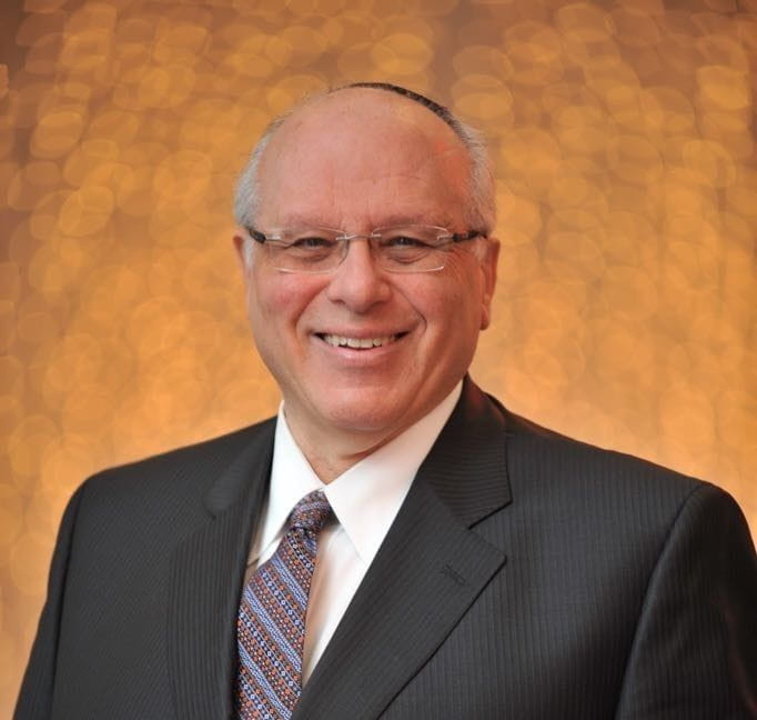 Moshe Meirovich smiles at the camera. He is wearing glasses and a suit.