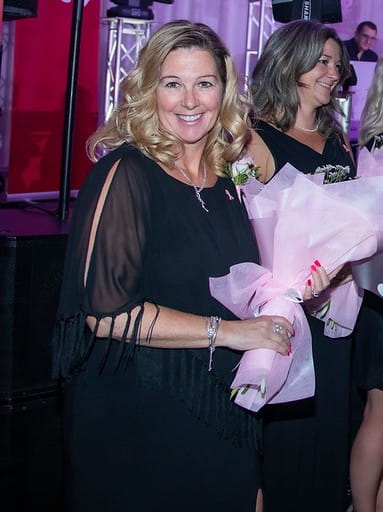 Sonia, souriante, qui tient un bouquet de fleurs avec ses collègues devant une scène.