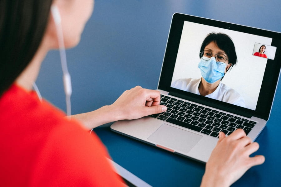 A person on a video call on their laptop. The person on the screen wears a face mask.