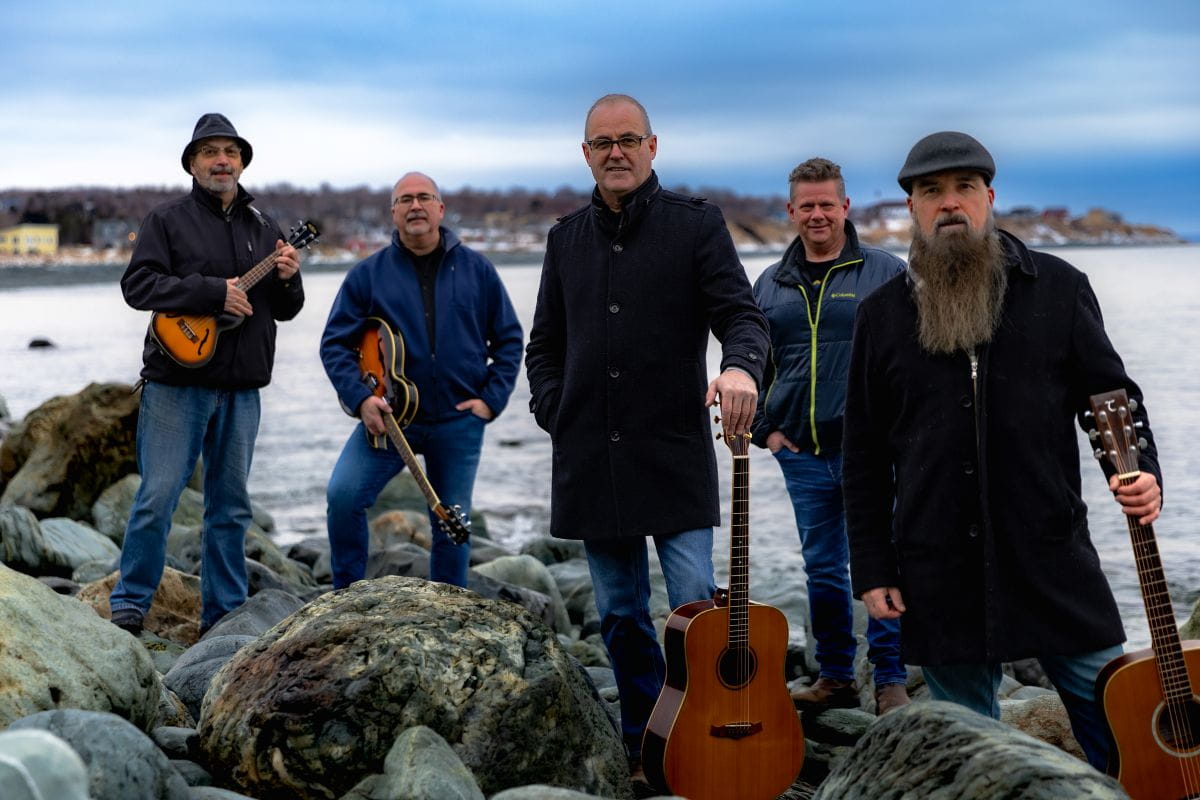 Wylie et les quatre autres membres de son groupe de musique, debout devant la rive, leurs instruments de musique à la main.