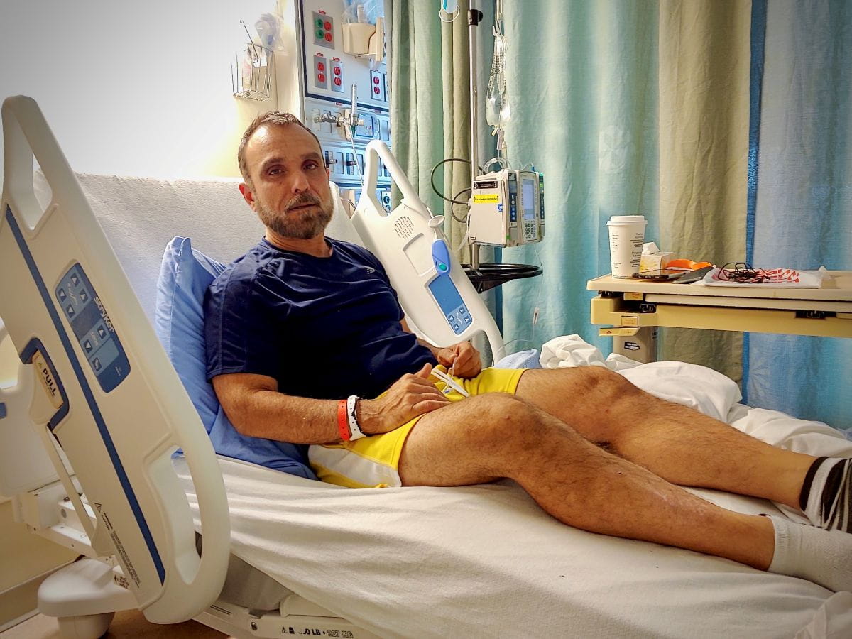 John Zeus Tokatlidis assis sur un lit d’hôpital.