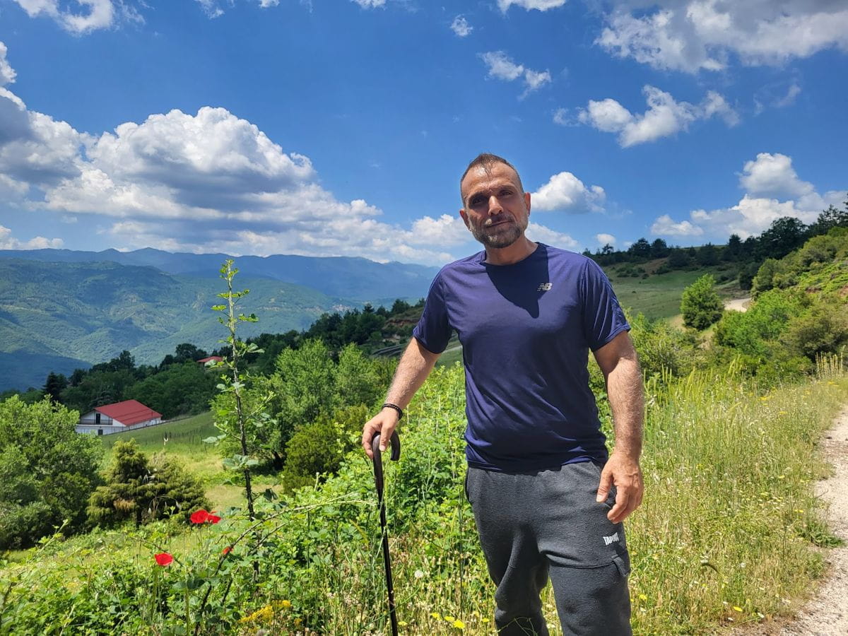 John Zeus Tokatlidis marche dans une vallée, avec des montagnes en arrière-plan.