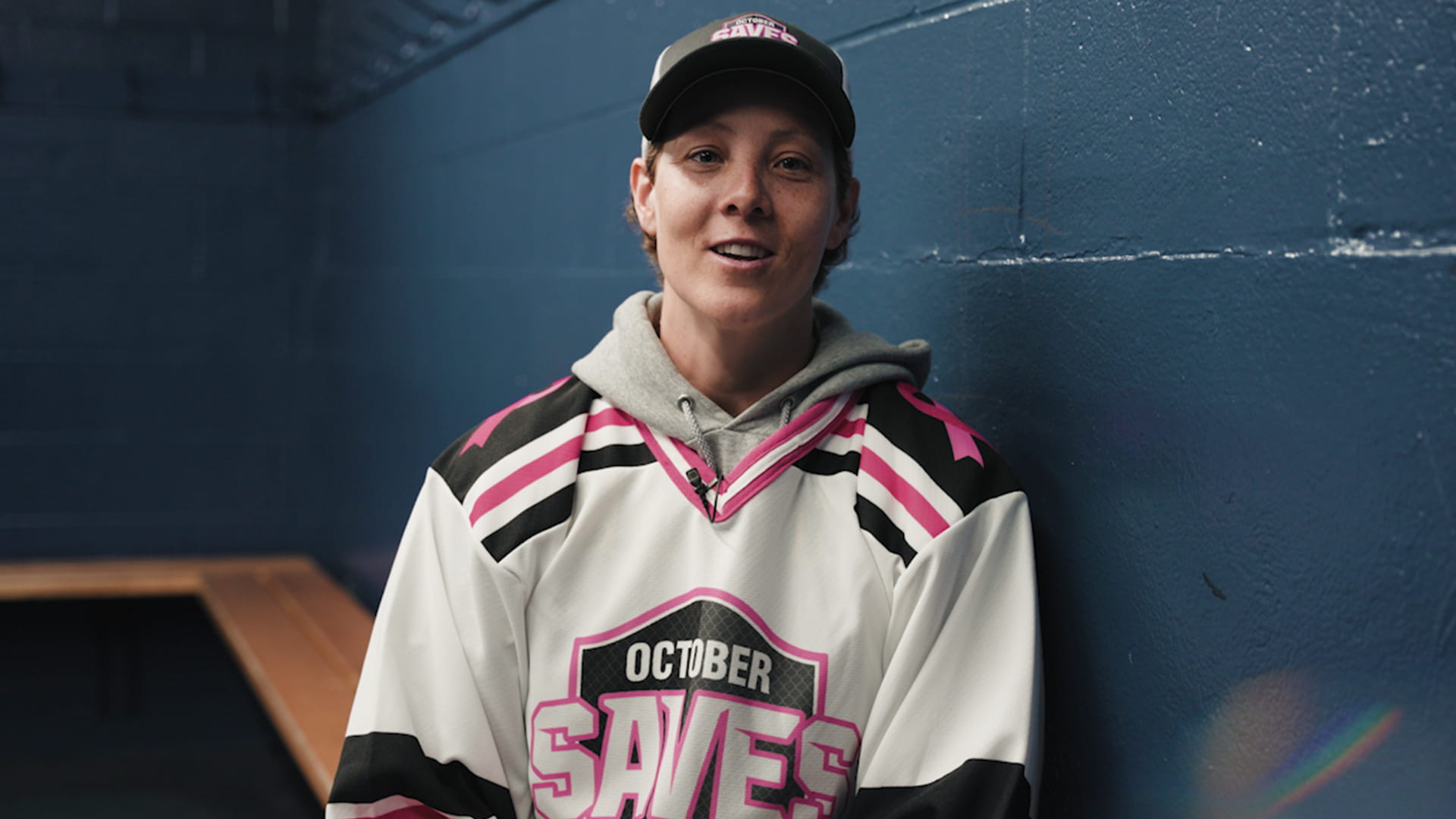 Erica Howe sitting on a bench in a locker room wearing an October Saves hockey jersey