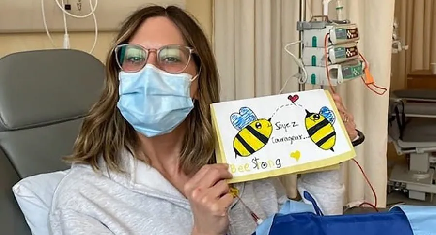 Amélie sitting in a hospital bed and is showing a drawing with the words “be strong”