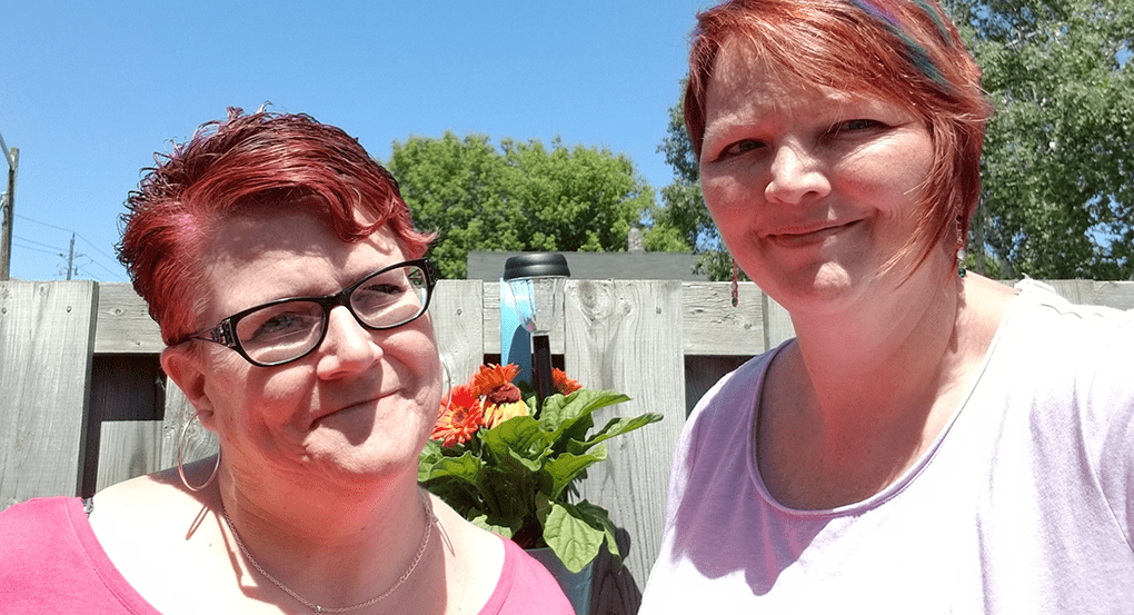 (left) Paula Pestrin and (right) Sandra de Haan standing together outside together in front of a fence. 