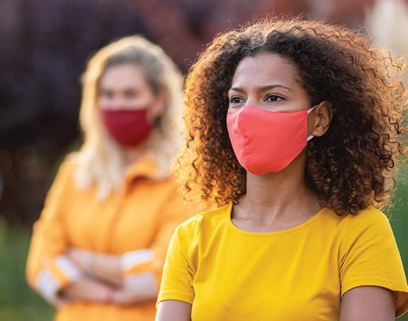Two people wearing face masks outside looking into the distance.