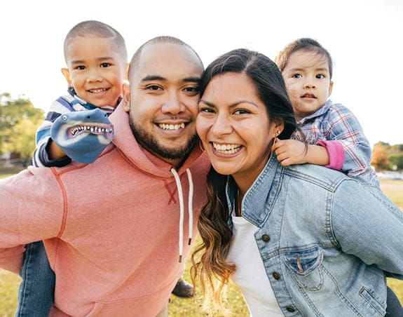 A mother and father carrying their son and daughter on their backs and smiling