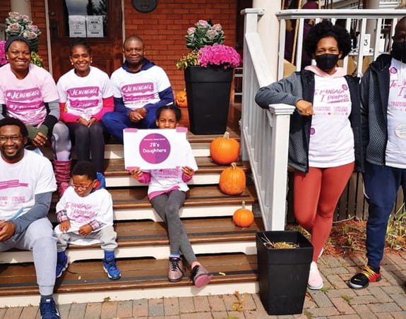 Eight people, adults and children, wearing matching CIBC Run for the Cure t-shirts in front of a house