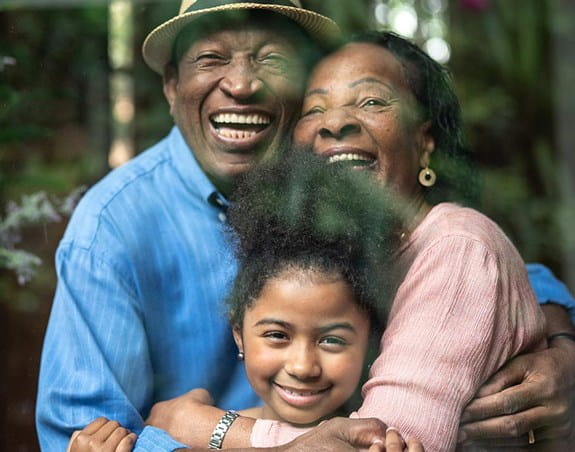Deux parents enlaçant leur fille en souriant à la caméra.
