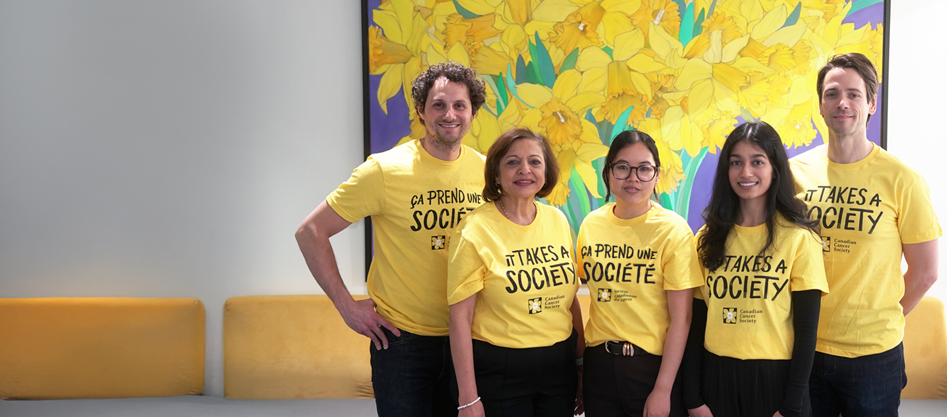 A group of five people wearing matching yellow “It Takes a Society” / « Ça prend une société » shirts pose together