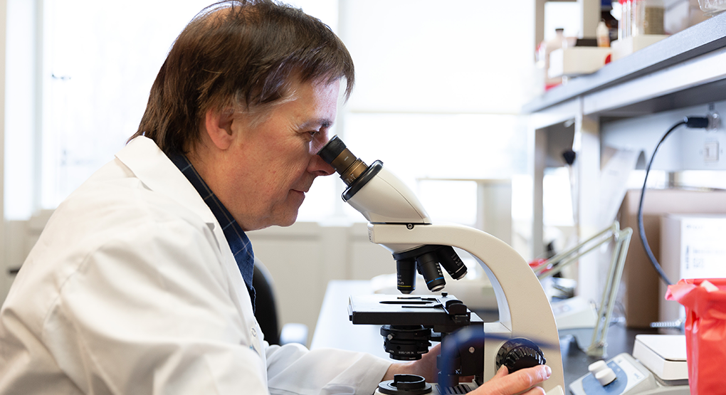 A scientist in a lab coat looks through a microscope at a laboratory workstation.