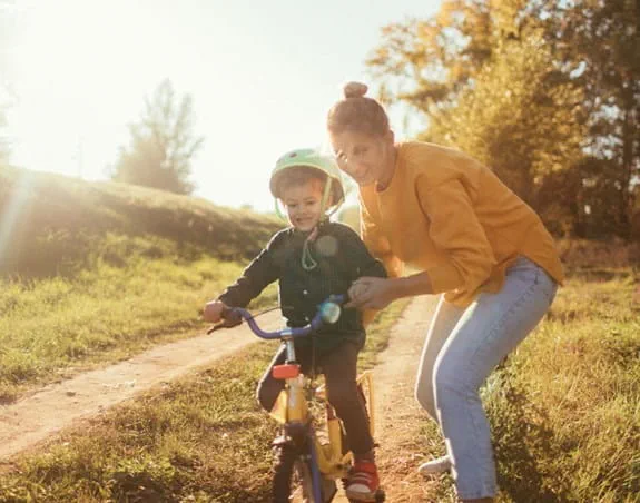 A young girl learning to ride her bike, mother helping her.