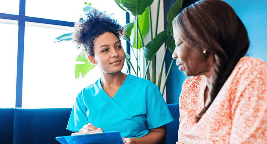 Healthcare professional writing on a clipboard with a patient in a clinic waiting room
