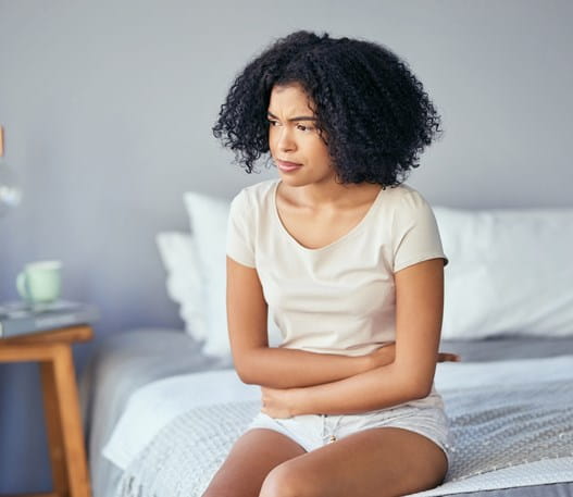 Patient sitting on a bed holding their stomach looking concerned